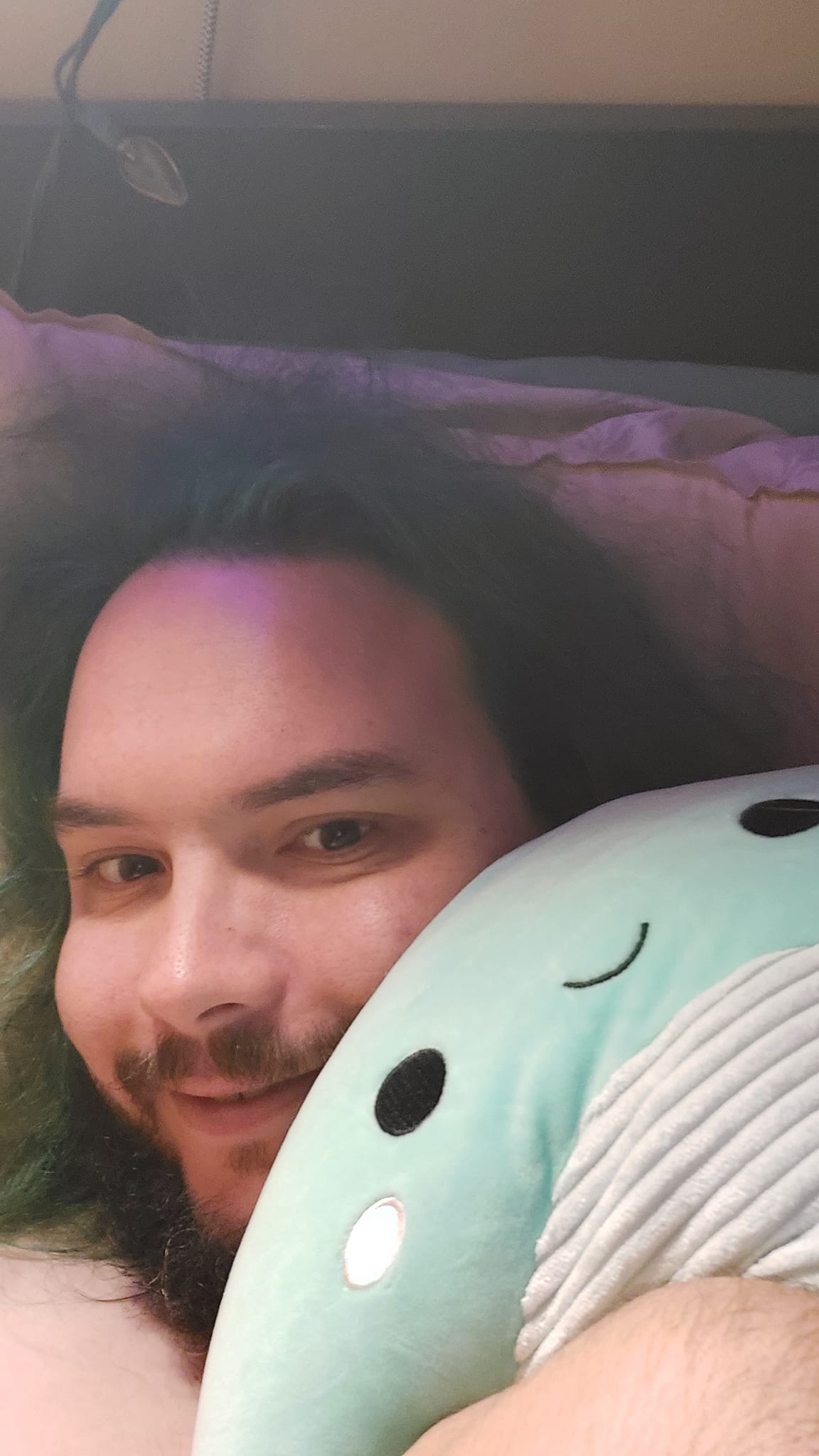 A man with green hair is holding a green Nessie Squishmallow, photo 1